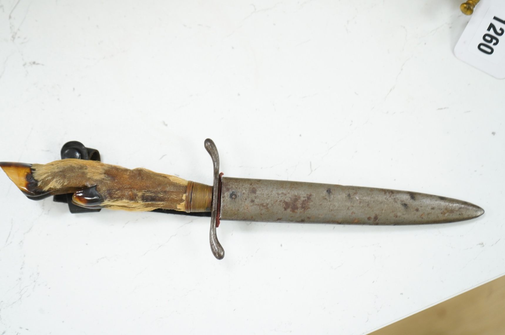 A First World War German Deer Hoof Fighting Knife, with a deer’s hoof grip, brass ferrell and steel cross guard, in original steel scabbard with leather belt loop mount, single edged blade with makers mark to one side; M